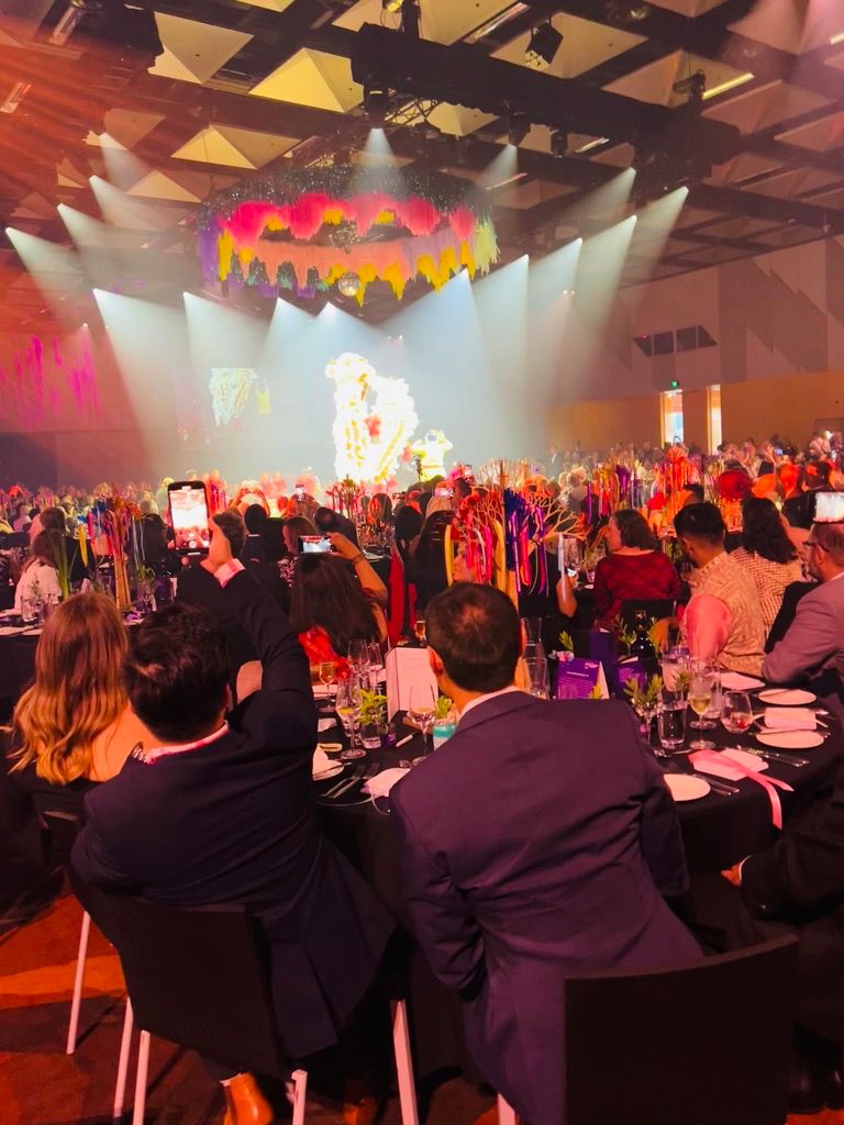 Guests seated at a large conference gala dinner with stage lighting and floral centrepieces