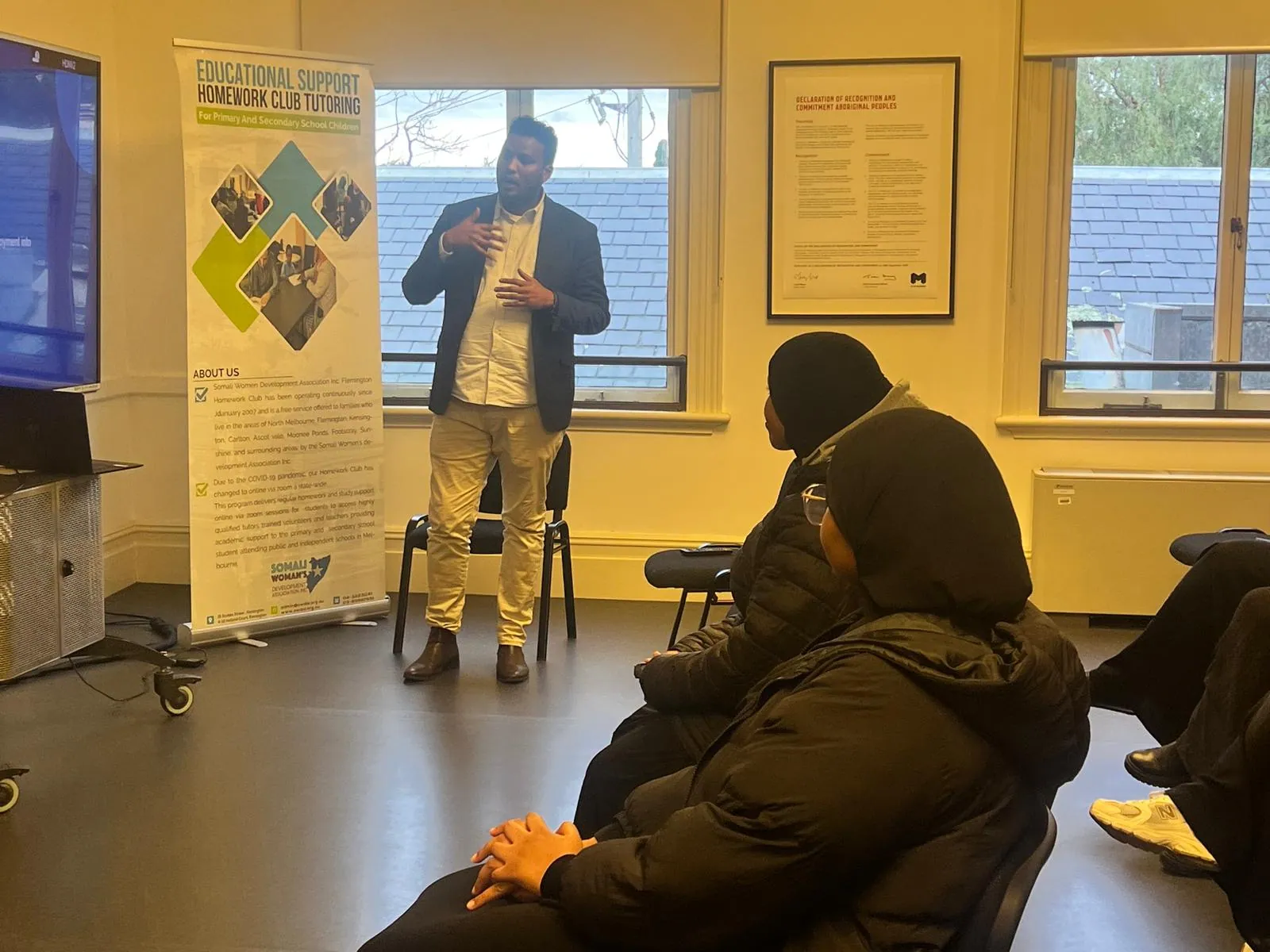 SWDA facilitator speaking to workshop participants beside the Homework Club tutoring banner