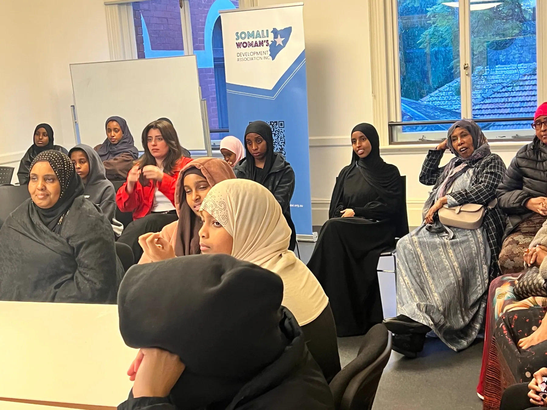 Workshop attendees listening beside the Somali Women's Development Association banner