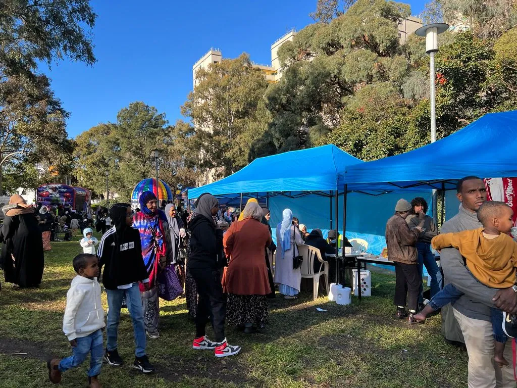 Blue SWDA marquees and community stalls at a multicultural festival in the park