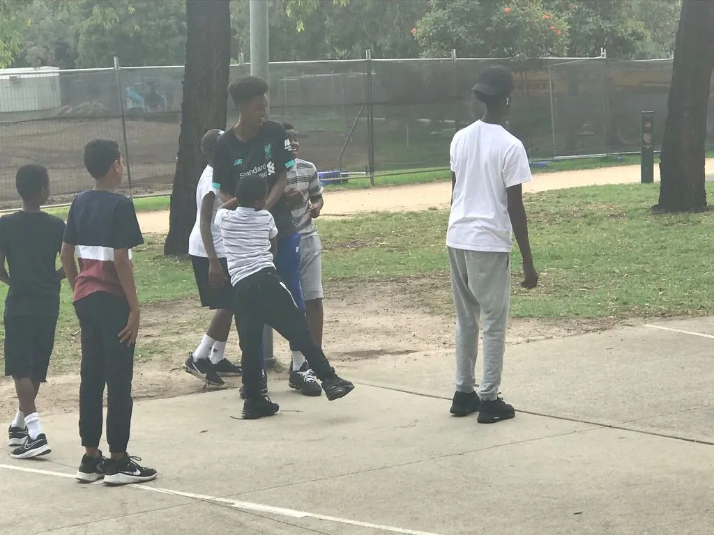 Young people playing basketball together at a school holiday activity in the park
