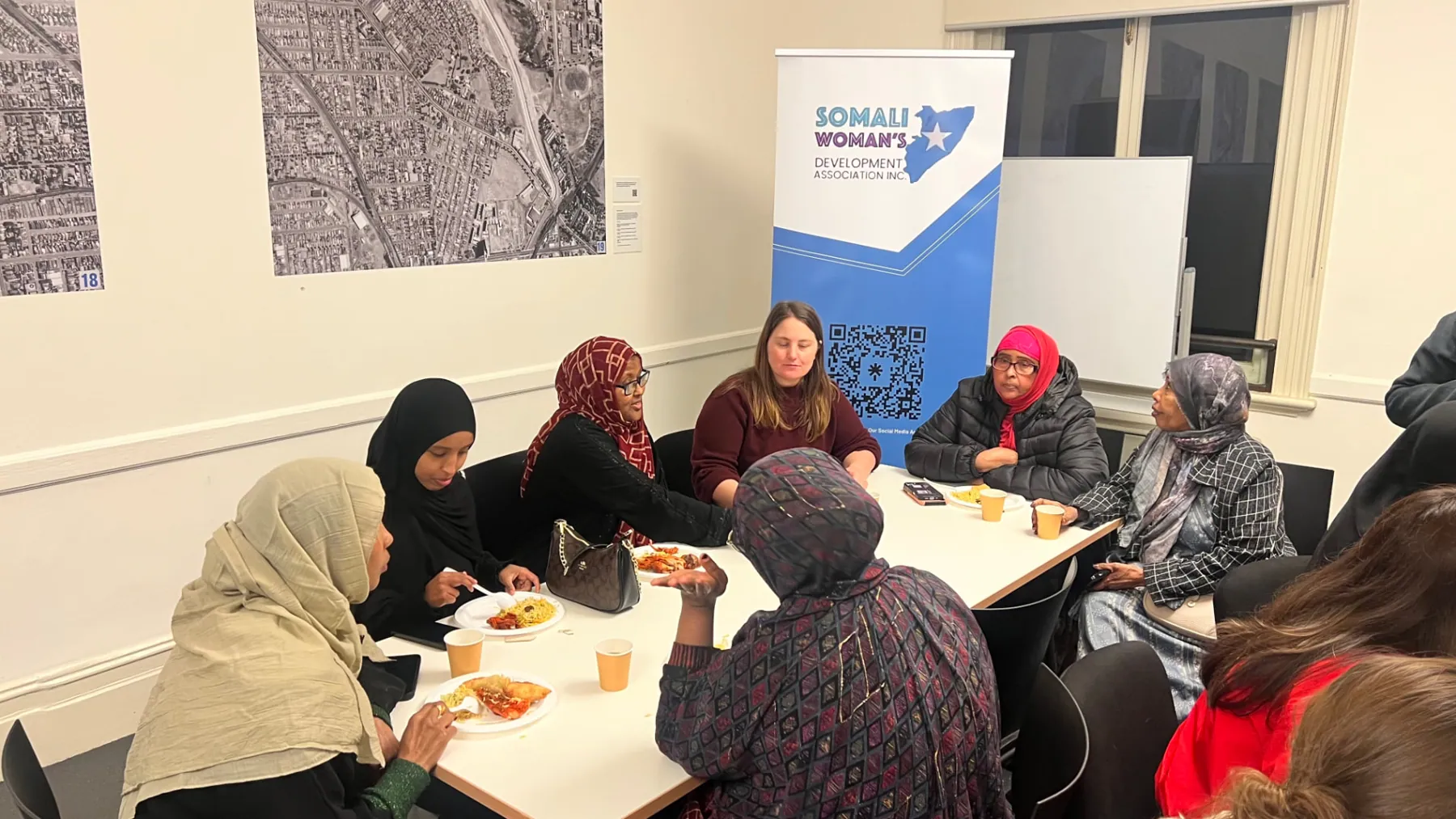 Women and guests eating together beside SWDA banners at a community session